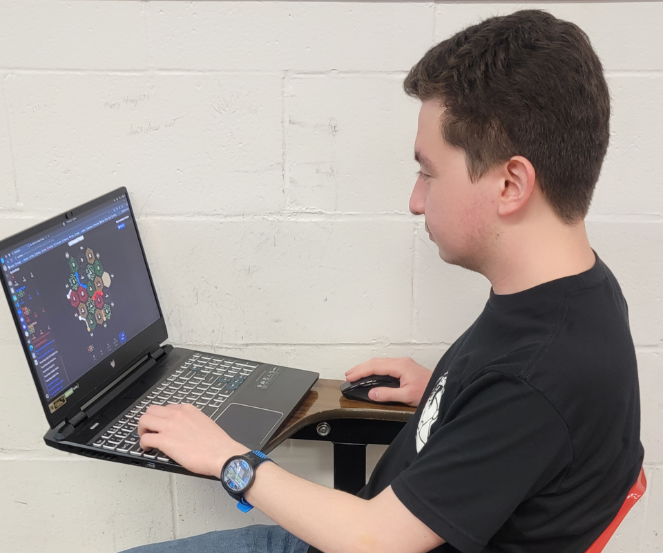 Brian sitting at a desk working on his computer with Catan on the screen.